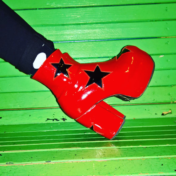 Red Patent Leather Platform Circus 70's Boots with Black Stars Modelled on a Green Bench